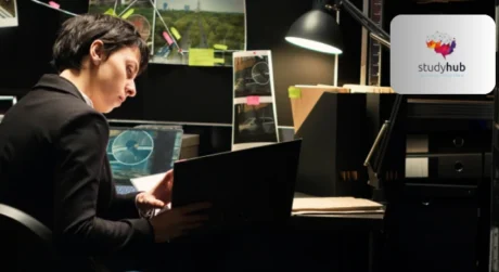 Professional researcher analyzing data on a laptop at a modern workspace with charts and documents.