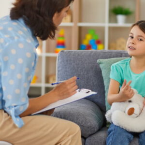 Young child sitting on a sofa talking with a professional during a one-on-one conversation in a comfortable indoor setting.
