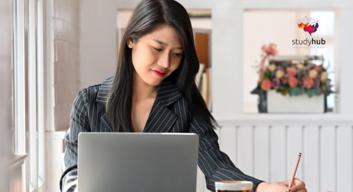 Young professional woman working on a laptop while taking notes at a desk in a bright workspace