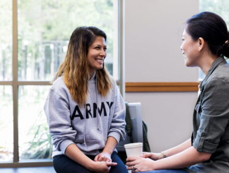Two women having a supportive one-on-one conversation indoors, seated and smiling during a casual counseling or mentoring session.