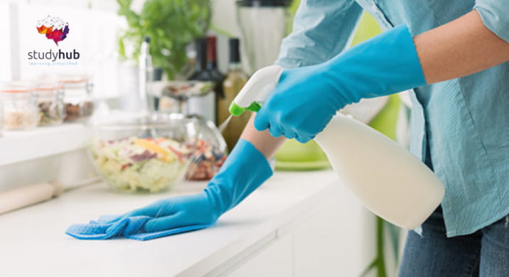 Person wearing blue gloves cleaning a kitchen countertop with a spray bottle and microfiber cloth.