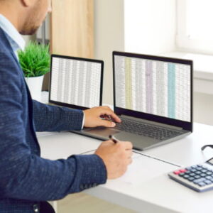 Professional working at a desk with a laptop, tablet, and calculator while analyzing data.