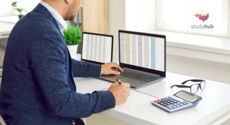Professional working at a desk with a laptop, tablet, and calculator while analyzing data.