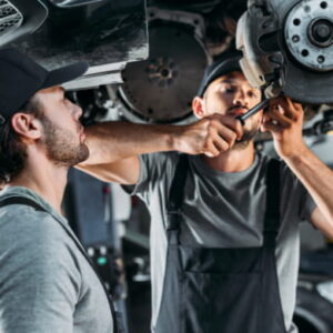 Two mechanics working together to repair a car in an automotive workshop.