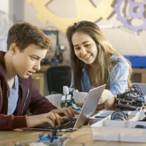 Young student learning robotics and coding on a laptop with guidance from a teacher in a classroom setting.