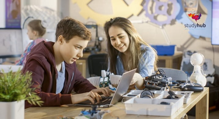 Young student learning robotics and coding on a laptop with guidance from a teacher in a classroom setting.