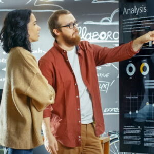 Two professionals analyzing business performance data on a digital dashboard with charts and graphs in a modern workspace.