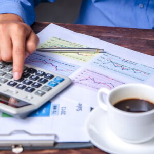 Accountant calculating product costs and analyzing financial charts with a calculator on a wooden desk.