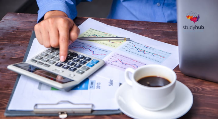 Accountant calculating product costs and analyzing financial charts with a calculator on a wooden desk.