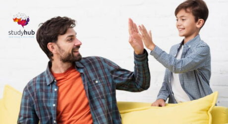 Father and son sitting on a couch giving each other a high five, showing positive bonding and encouragement at home.
