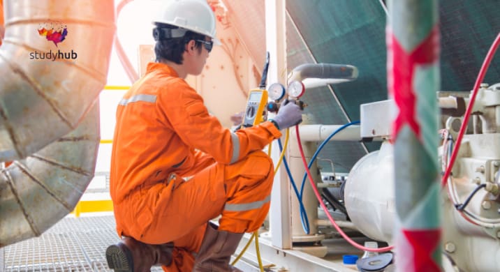 Industrial technician in orange protective coveralls inspecting pressure gauges on mechanical equipment.