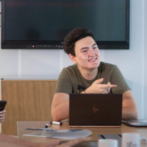 Young professional leading a team discussion during a meeting while using a laptop in a modern office.
