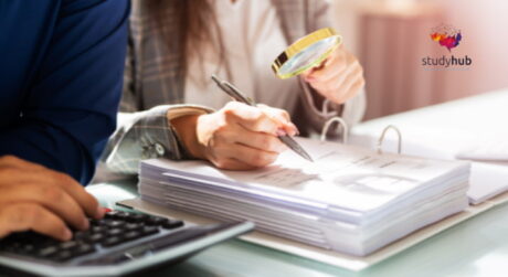 Professionals reviewing financial documents with a magnifying glass, calculator, and paperwork on an office desk.
