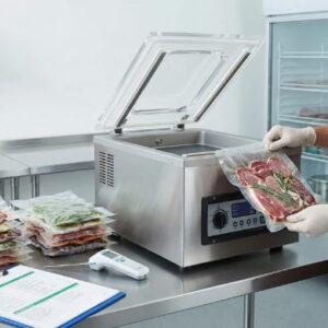 Professional food handler using a commercial vacuum packing machine to seal fresh ingredients in a kitchen.