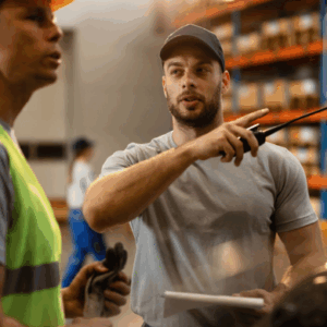 Supply chain manager directing a warehouse worker in a stocked distribution center.