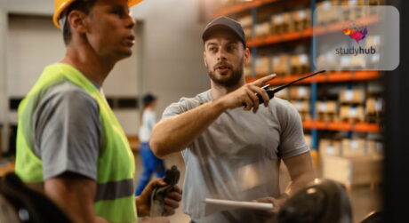 Supply chain manager directing a warehouse worker in a stocked distribution center.