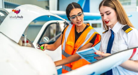 Two women inspecting an aircraft engine, with an aviation technician explaining procedures to a pilot during maintenance training.