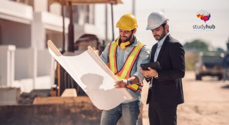 Construction engineers reviewing building plans at an active construction site while wearing safety helmets.