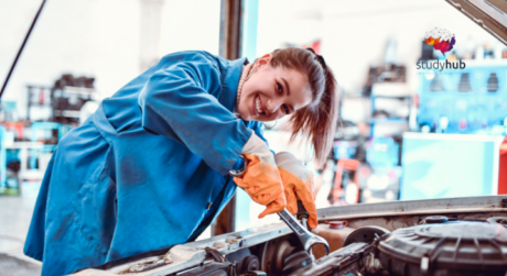 Smiling female mechanic in blue uniform using a wrench to repair a car engine in an auto workshop