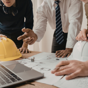Construction team reviewing blueprints with safety helmets and laptop on desk during project planning
