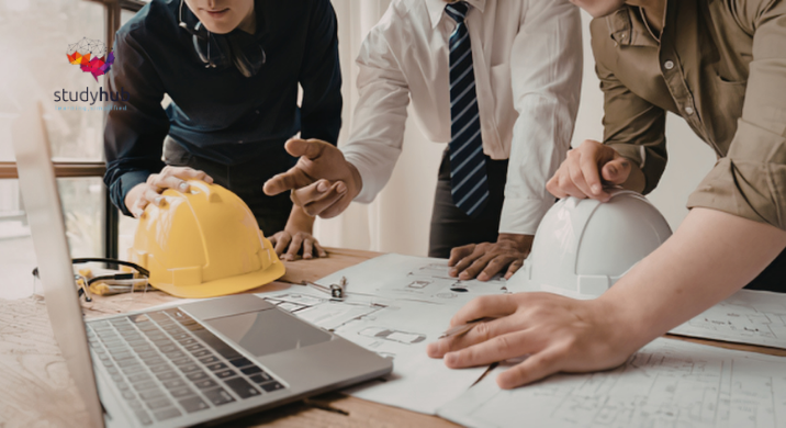 Construction team reviewing blueprints with safety helmets and laptop on desk during project planning
