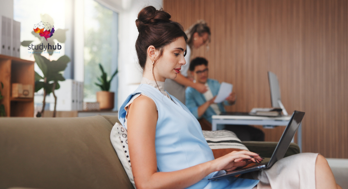 Pregnant woman working on a laptop from home while colleagues collaborate in the background