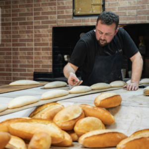 Baker preparing fresh bread dough in a bakery, shaping loaves on a floured work surface