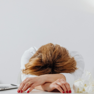Exhausted woman resting head on desk beside laptop showing signs of workplace stress and burnout