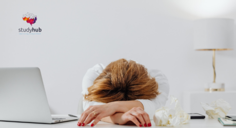 Exhausted woman resting head on desk beside laptop showing signs of workplace stress and burnout