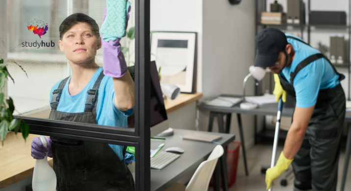 Professional cleaners in uniforms cleaning office space, one wiping glass window and another mopping floor