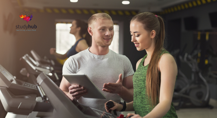 Personal trainer guiding a young woman on a treadmill while holding a tablet in a modern gym.