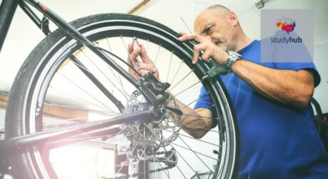 Professional bicycle mechanic repairing and adjusting the rear wheel and brake system of a bike in a workshop.
