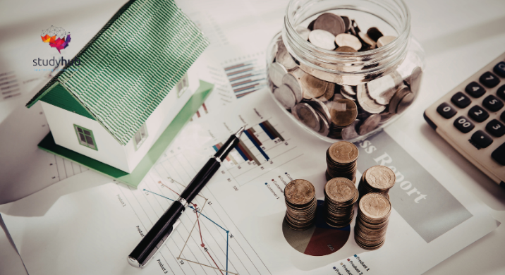 Coins stacked beside a glass jar, calculator, and model house on financial charts and reports