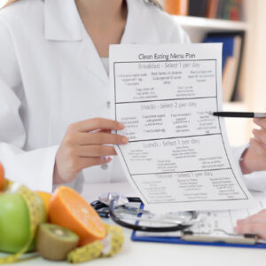 Nutritionist holding a clean eating meal plan and explaining diet chart to a client with fresh fruits on table
