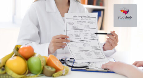 Nutritionist holding a clean eating meal plan and explaining diet chart to a client with fresh fruits on table